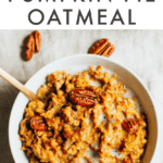 Bowl of pumpkin pie oatmeal with almond milk and pecans on top. Spoon in bowl and pecans scattered around the bowl.