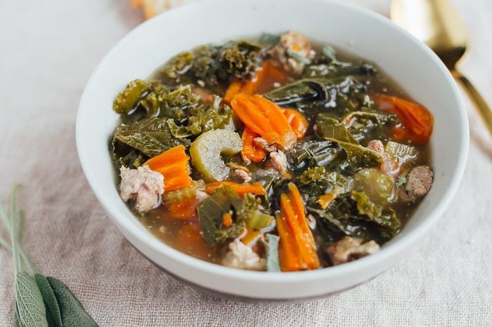 A bowl of kale and sausage soup in a white bowl.