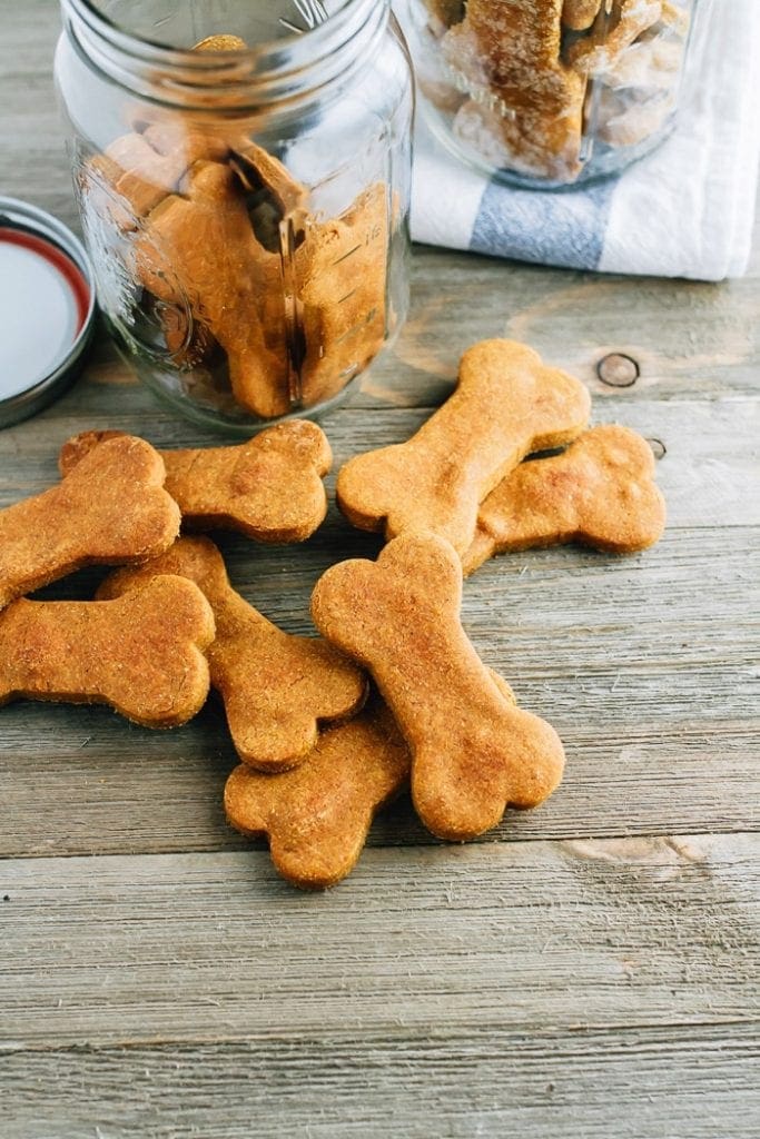 Peanut Butter and Pumpkin Dog Treats on a wood table next to a mason jar filled with more bone-shaped dog treats.