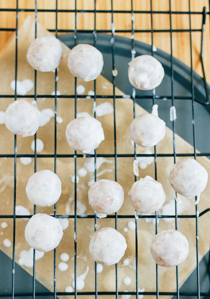 Pumpkin size donut holes on a rack over parchment paper, being glazed with the coconut frosting.