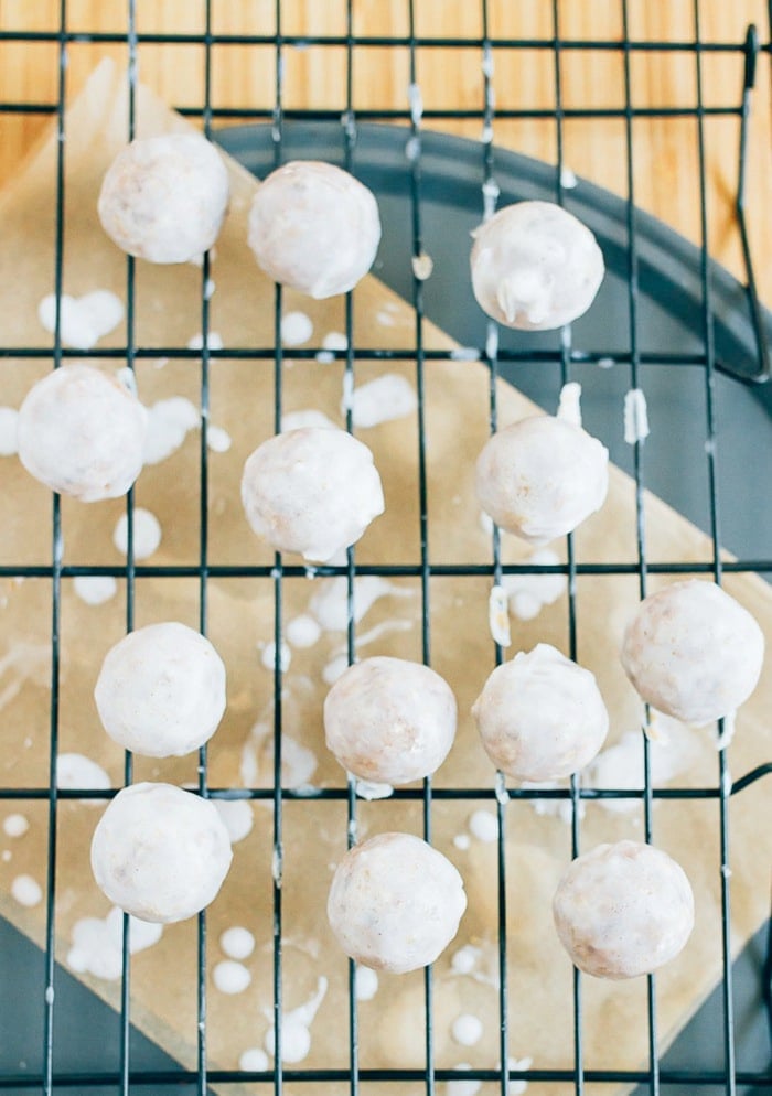 Pumpkin size donut holes on a rack over parchment paper, being glazed with the coconut frosting.