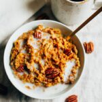 Overhead shot of Slow Cooker Pumpkin Pie Oatmeal in a white bowl with milk and pecans in the bowl.