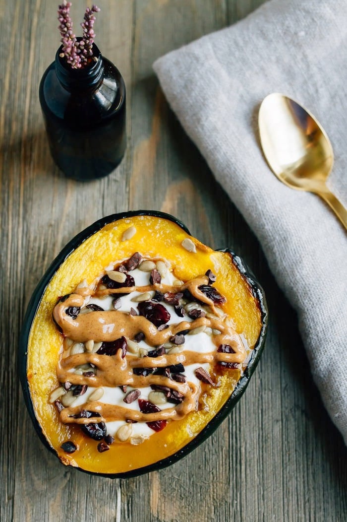 Roasted acorn squash breakfast bowls served warm with yogurt and cranberries and seeds, and a peanut butter drizzle.