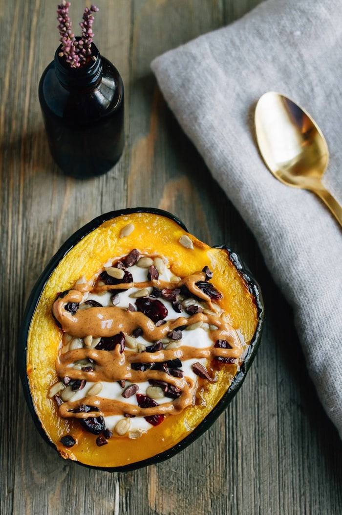 Roasted acorn squash breakfast bowls served warm with yogurt and cranberries and seeds, and a peanut butter drizzle.