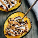 2 acorn squash breakfast bowls with a spoon, filled with yogurt, sunflower seeds, dried cranberries, and drizzled with peanut butter.