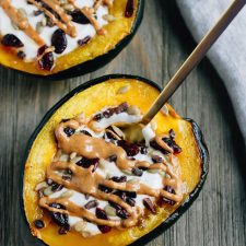 2 acorn squash breakfast bowls with a spoon, filled with yogurt, sunflower seeds, dried cranberries, and drizzled with peanut butter.