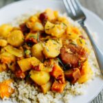 Root vegetable tagine over quinoa on a white plate with a fork.