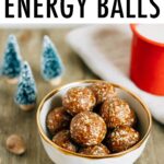 Bowl of gingerbread energy balls on a table with mini Christmas trees and a red enamel mug of milk.