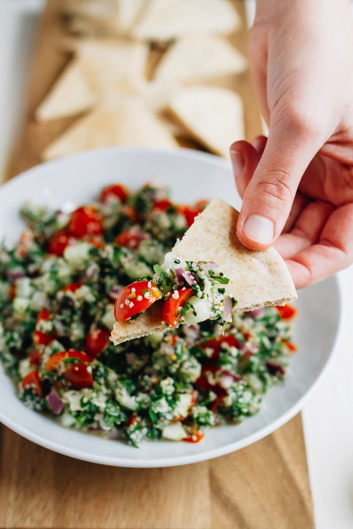 Hand dipping a pita triangle into a bowl of hemp heart tabbouleh.