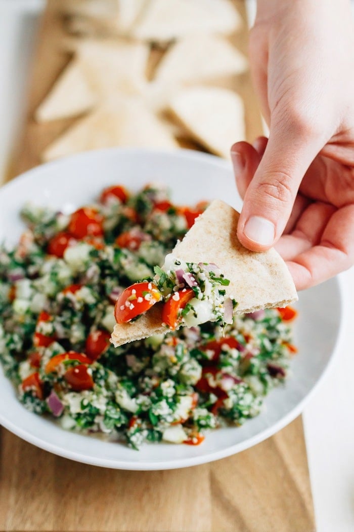 Hand dipping a pita triangle into a bowl of hemp heart tabbouleh.