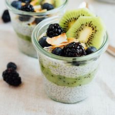 Two cups of kiwi chia pudding parfait, topped with blackberries, blueberries, shredded coconut, and sliced kiwi.