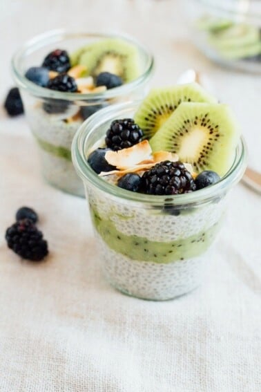 Two cups of kiwi chia pudding parfait, topped with blackberries, blueberries, shredded coconut, and sliced kiwi.