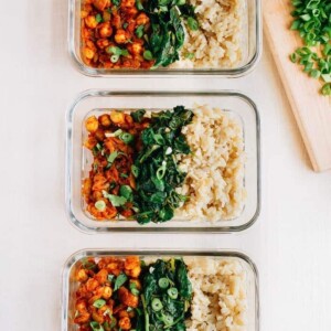 Three glass containers, each with rows of curried chick peas, garlic sautéed spinach, and white rice.