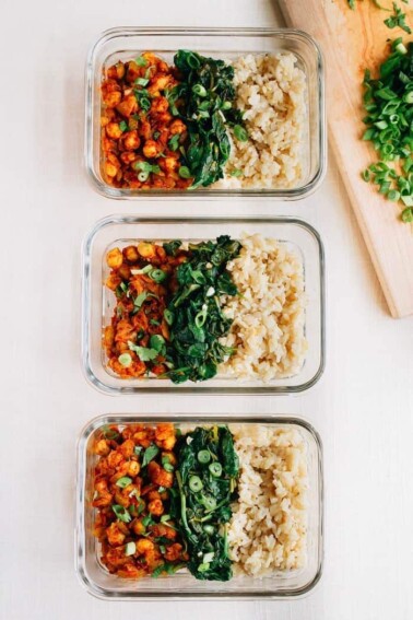 Three glass containers, each with rows of curried chick peas, garlic sautéed spinach, and white rice.