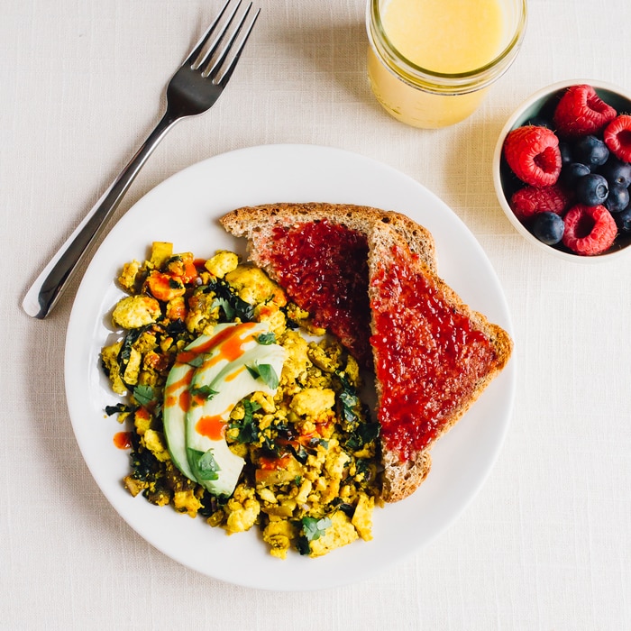 Turmeric tofu scramble on a plate with avocado on top. Two slices of bread with jam on the side. 