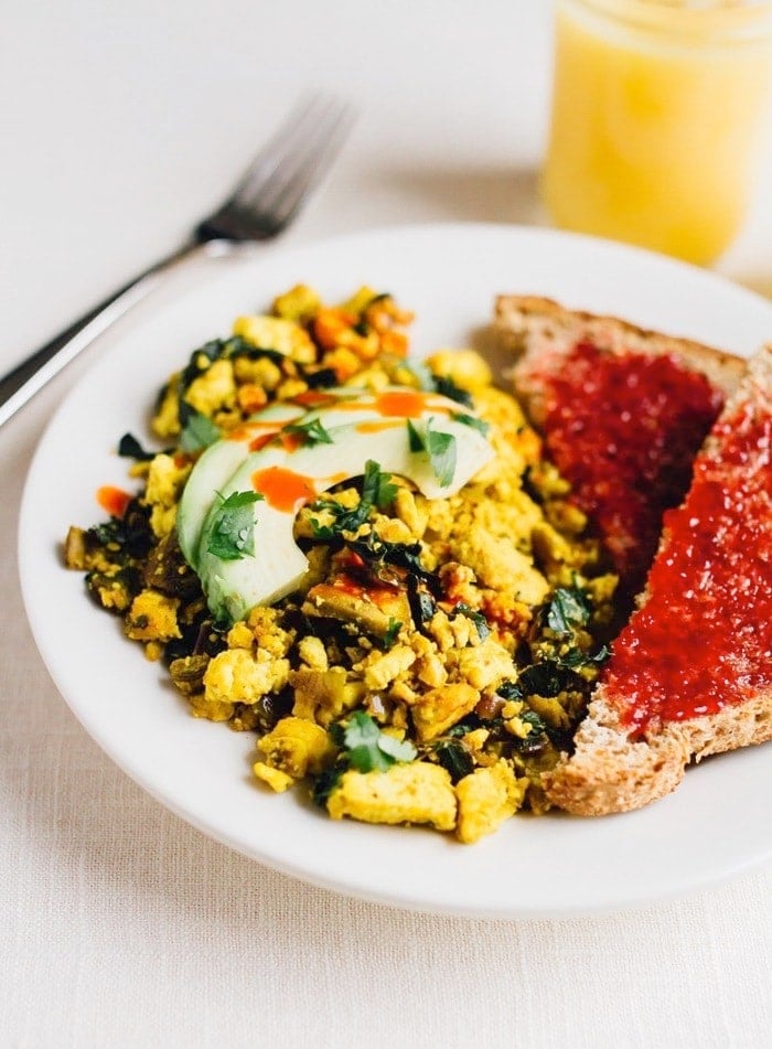 Turmeric tofu scramble on a plate with avocado on top. Two slices of bread with jam on the side. 