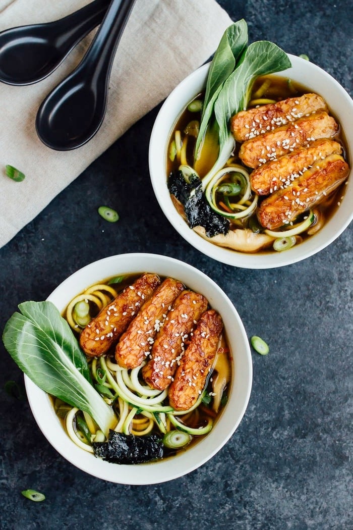 Overhead shot of vegan zucchini noodle ramen bowls served in white bowls on dark grey countertop.