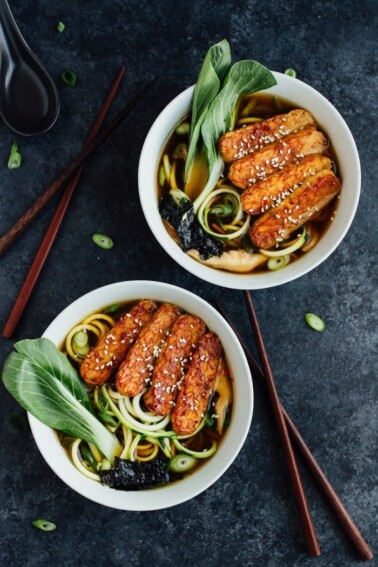 Two bowls of ramen made with tempeh, zucchini noodles, dried seaweed, and bok choy, with chopsticks on the table.