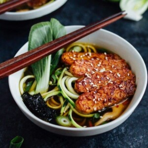 Two bowls of ramen made with tempeh, zucchini noodles, dried seaweed, and bok choy, with chopsticks on the bowl ledge.