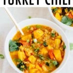 White bowl and spoon with turkey chili made with lentils, butternut squash and kale.