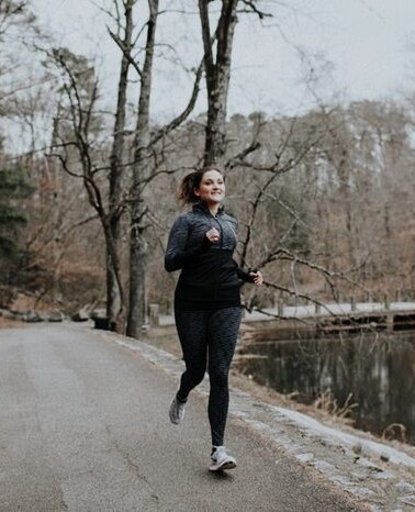 Woman running on a road next to a pond in all black athletic wear.