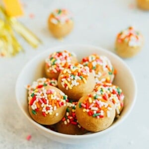 Vanilla cake balls with rainbow sprinkles in a small white bowl.