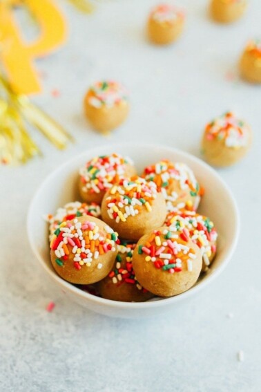 Vanilla cake balls with rainbow sprinkles in a small white bowl.