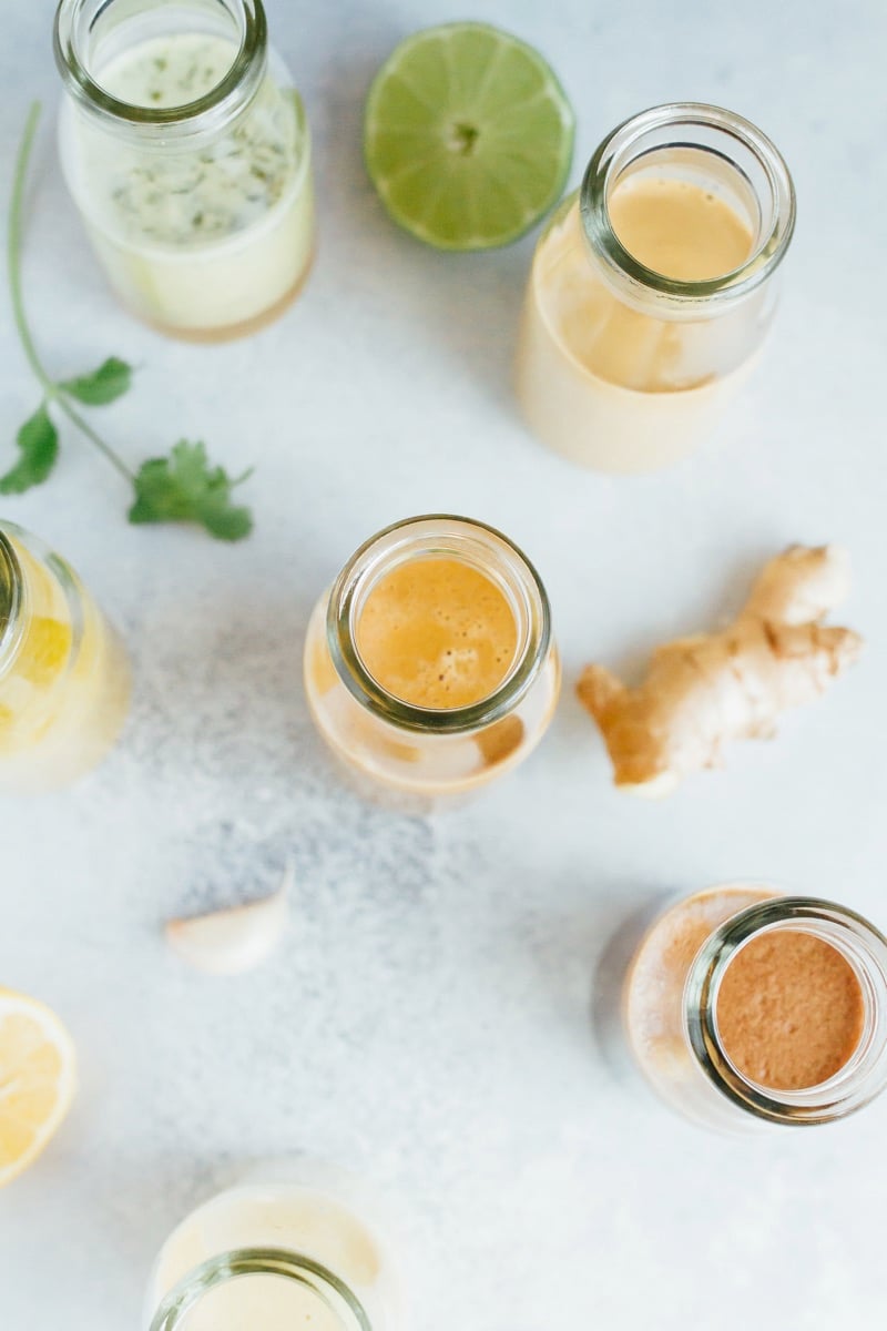 6 jars spread out on a grey countertop with a lime, ginger, cilantro, and garlic.