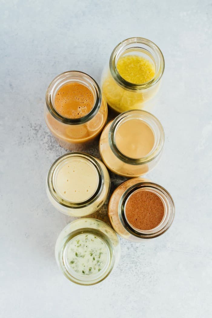 6 homemade dressings in glass jars on a gray countertop. 