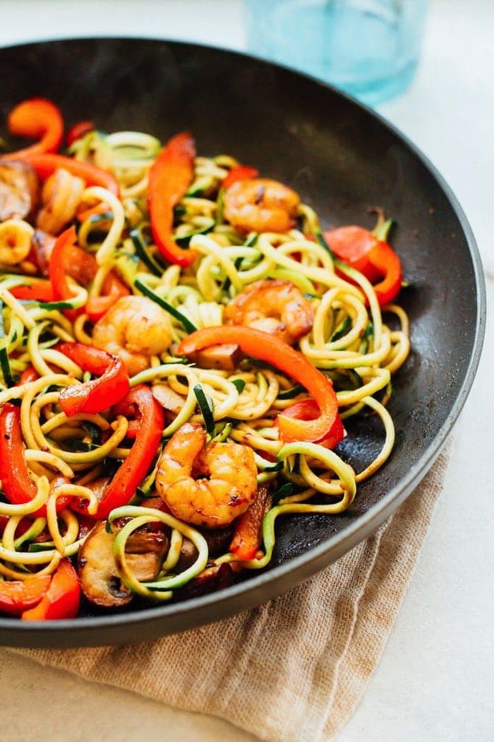 Up close shot of zucchini noodles and shrimp in a large skillet. 