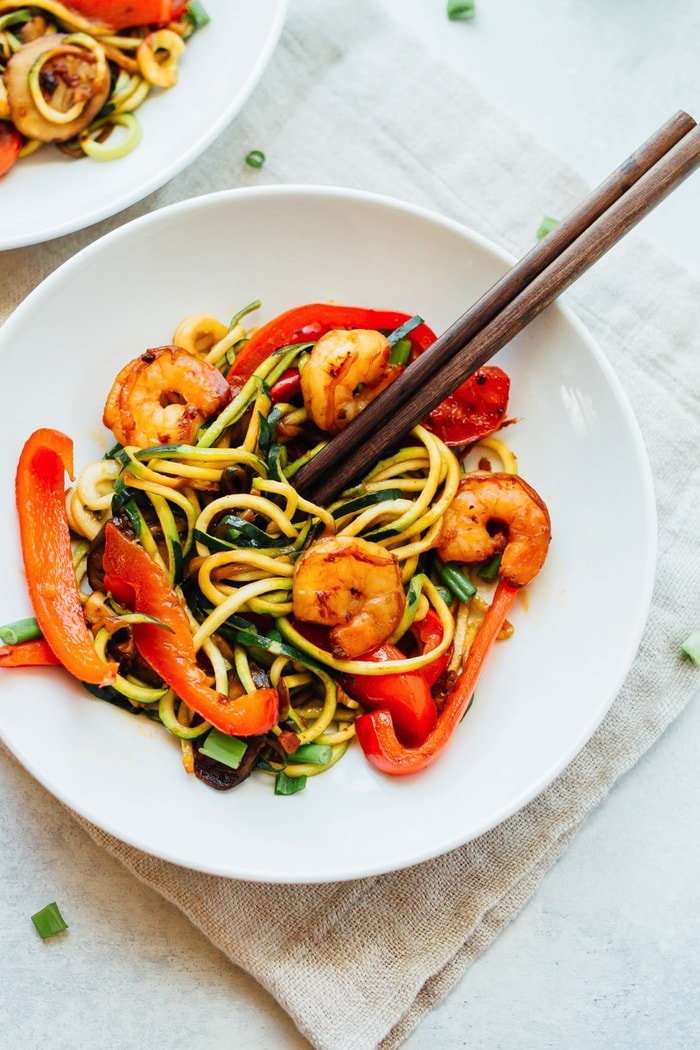 Zucchini noodle and shrimp lo mein in a bowl with wooden chopsticks. 