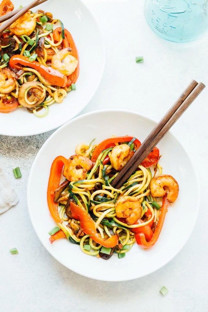 Zucchini noodle and shrimp lo mein in a white bowl with wooden chopsticks. 