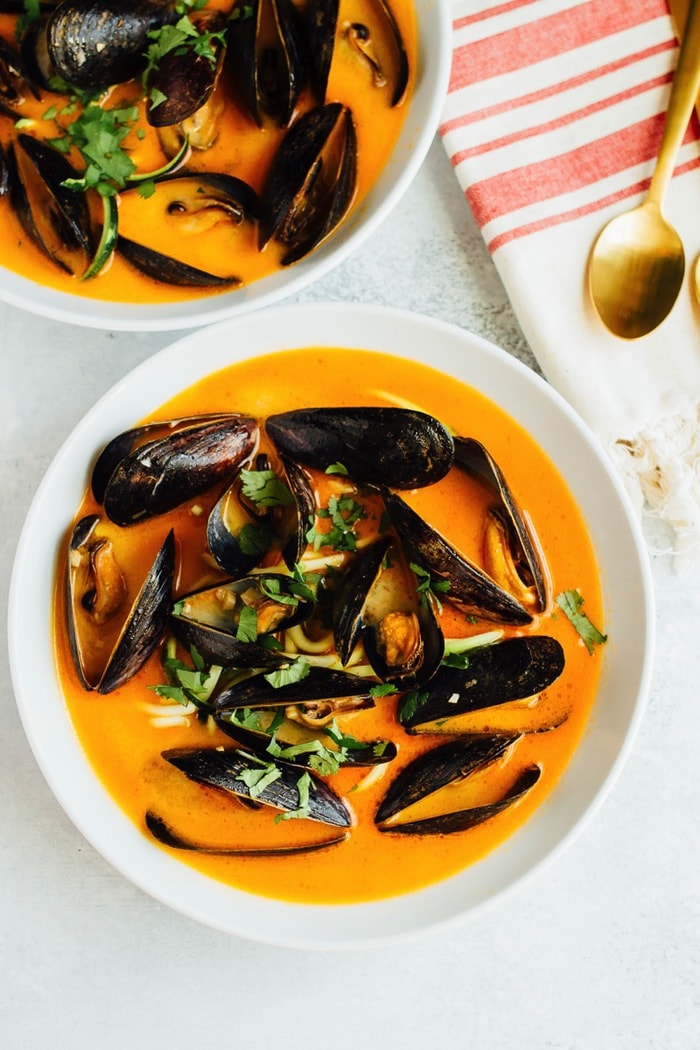 Two bowls of coconut curry mussels in a bowl with zucchini noodles and topped with cilantro.