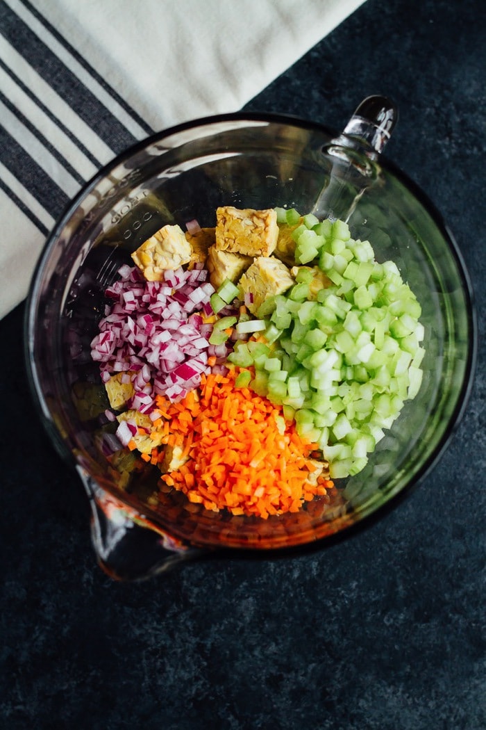 Curried Tempeh Salad Recipe Ingredients in a glass bowl -- tempeh, celery, carrots and onion.