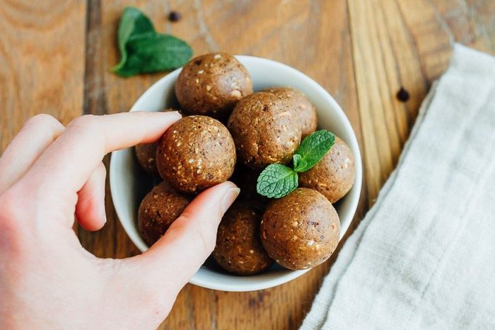 Two fingers grabbing a Thin Mint Protein Ball in a white bowl on wood cutting board with fresh mint leaves.