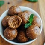 A bowl of thin mint protein balls with a bite taken out of one and fresh mint leaves.