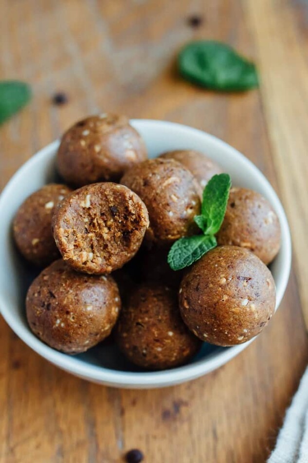 A bowl of thin mint protein balls with a bite taken out of one and fresh mint leaves.