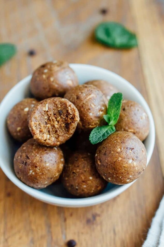 A bowl of thin mint protein balls with a bite taken out of one and fresh mint leaves.