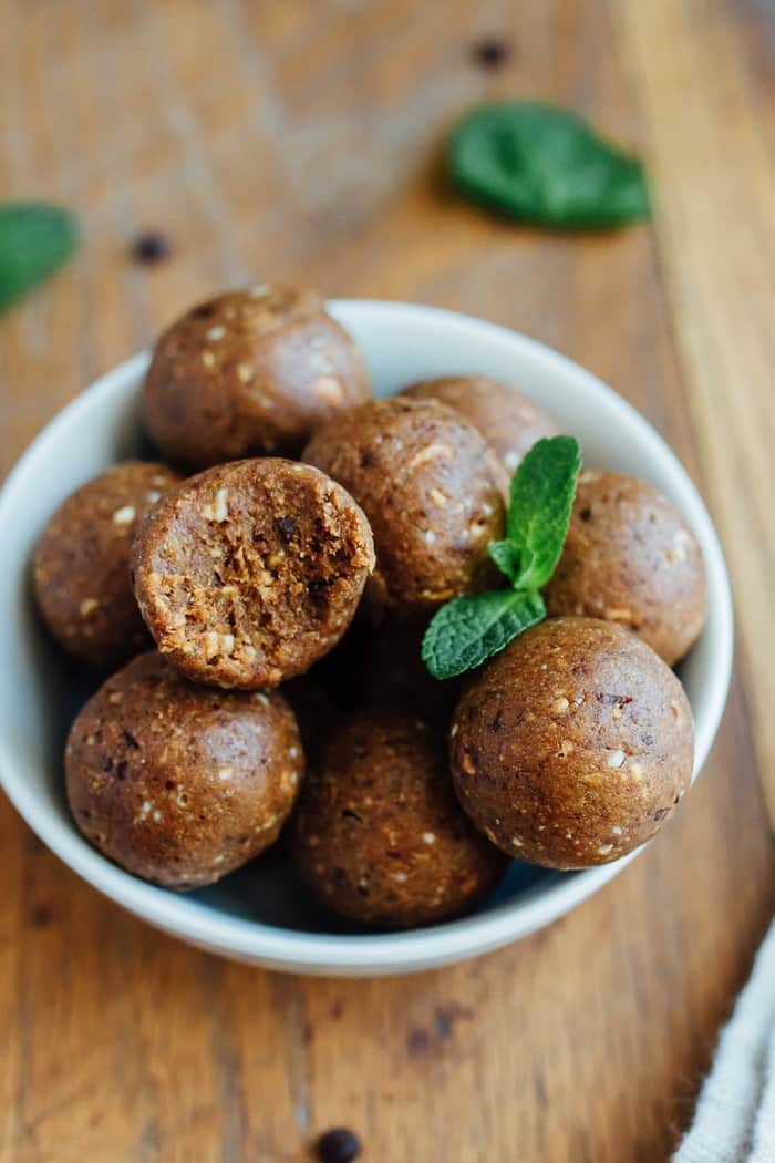 Thin Mint Protein Balls in a white bowl on wood cutting board with fresh mint leaves.