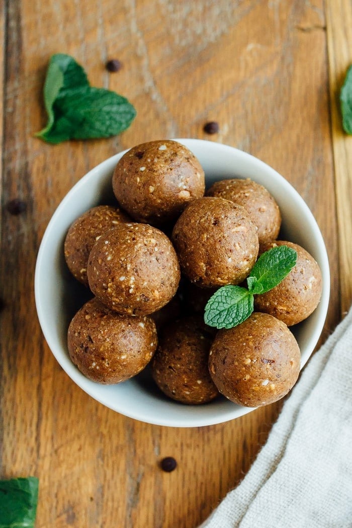 Thin Mint Protein Balls in a white bowl on wood cutting board with fresh mint leaves.