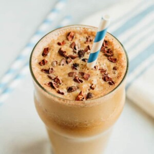 Cup of chocolate cauliflower smoothie topped with cacao nibs and a blue and white striped straw.