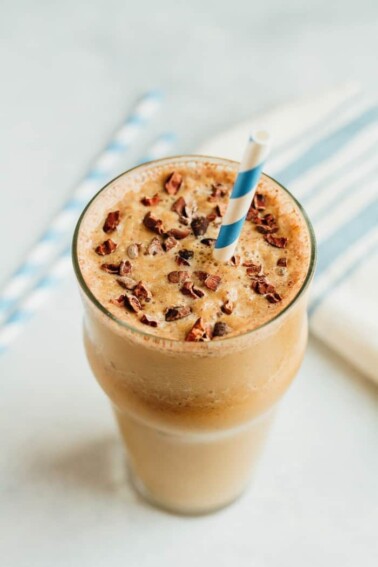 Cup of chocolate cauliflower smoothie topped with cacao nibs and a blue and white striped straw.