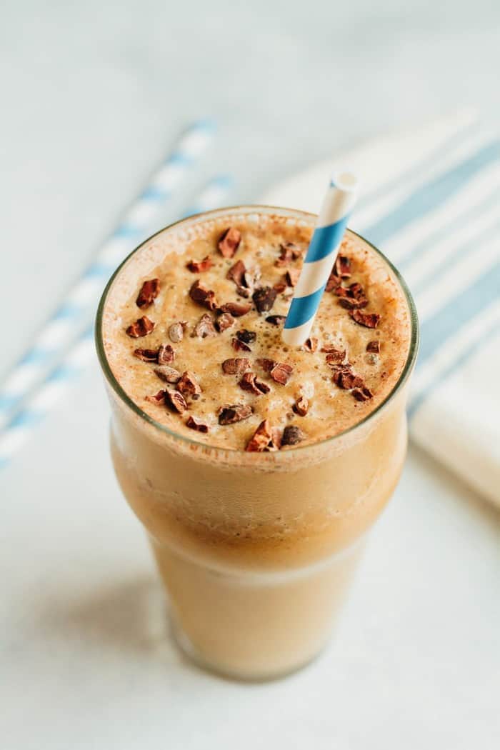 Glass of malted chocolate cauliflower smoothie with a blue and white striped straw.