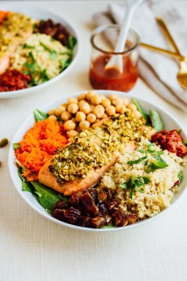 Close-up shot of Pistachio Crusted Salmon served over a bed of baby spinach with quinoa, chickpeas, carrots, dates and a spicy harissa dressing.