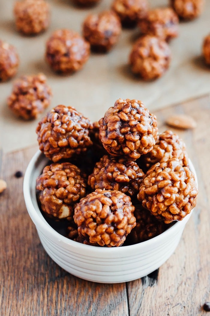 An overflowing bowl of chocolate almond crispy bites is in the foreground, with a additional bites in the background resting on top of parchment paper.