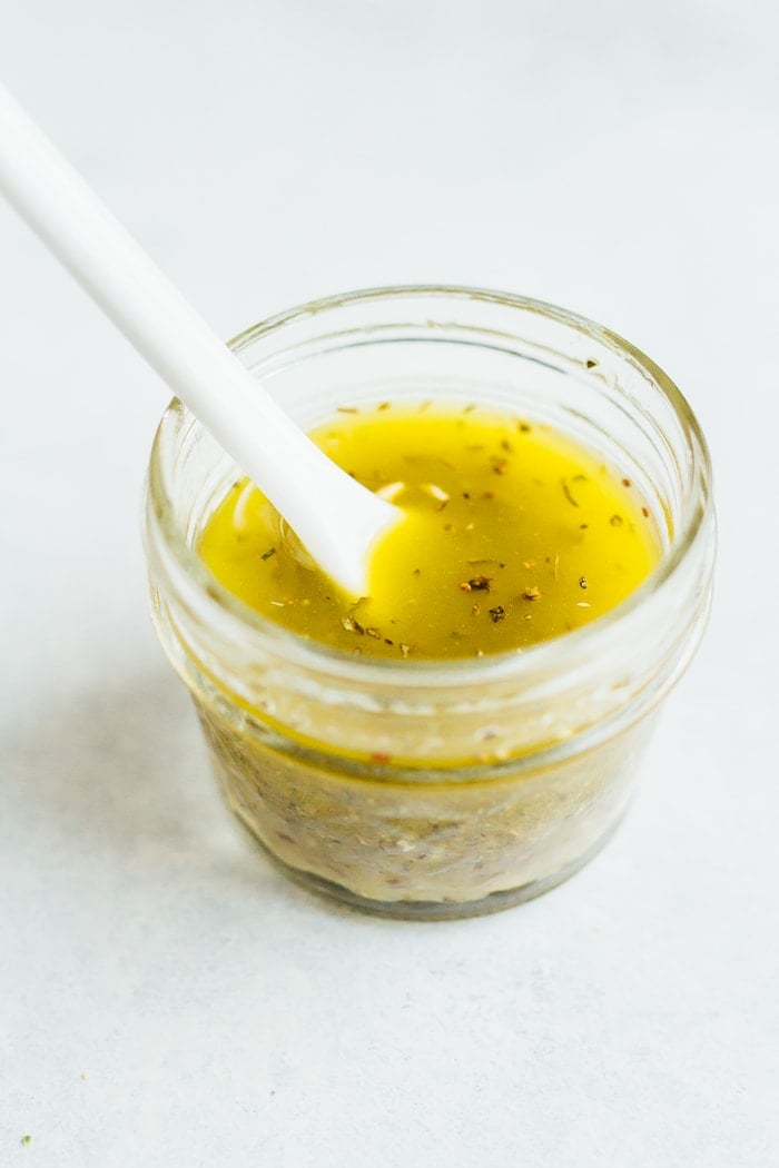Small mason jar containing lemon chia dressing with a mixing spoon.