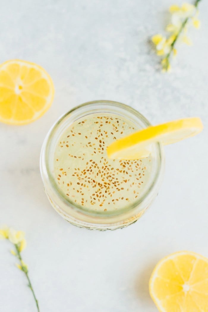 Overhead shot of Lemon Chia Fresca in clear mason jar with lemon slices and yellow flowers.