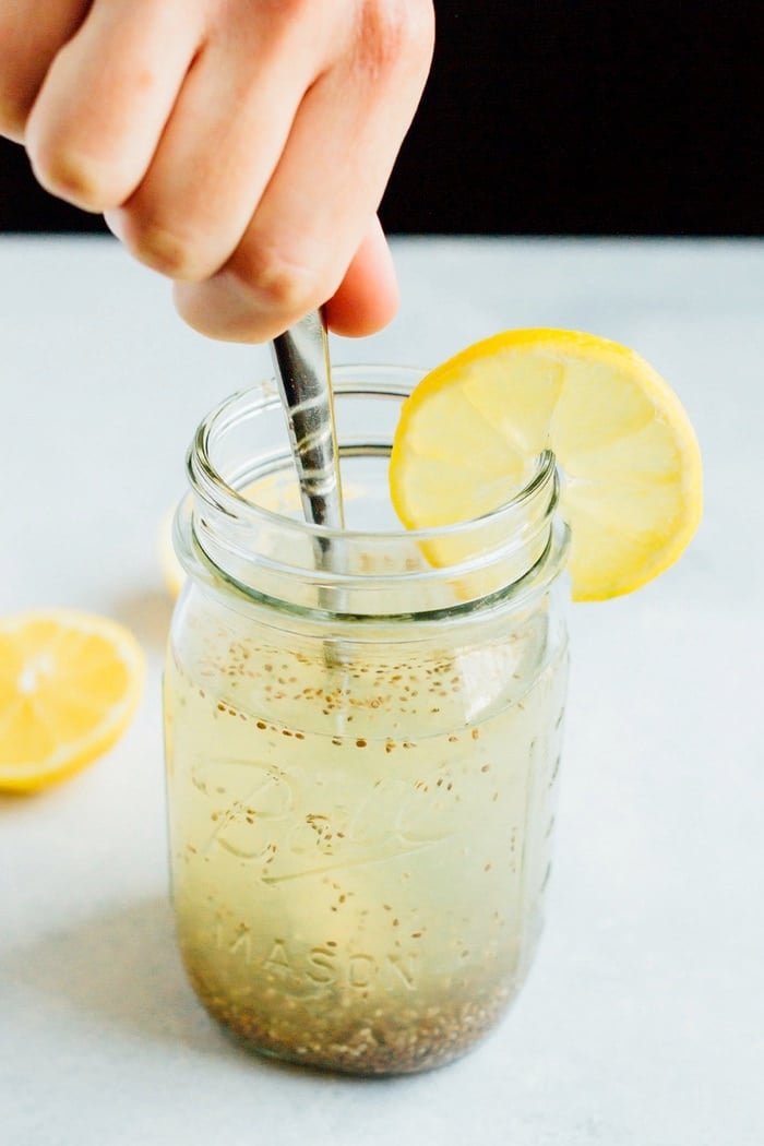 Hand stirring a spoon into a clear mason jar of Lemon Chia Fresca.