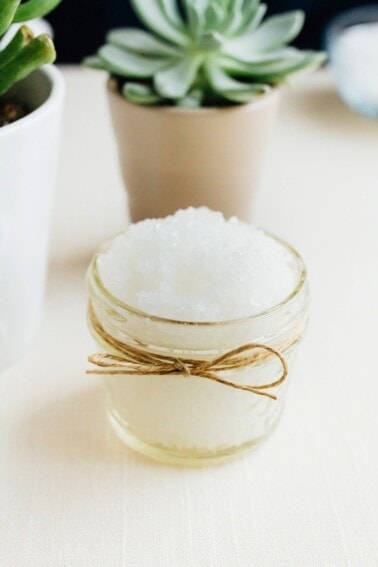 Small mason jar wrapped with twine and filled with peppermint foot scrub with succulents in the background.