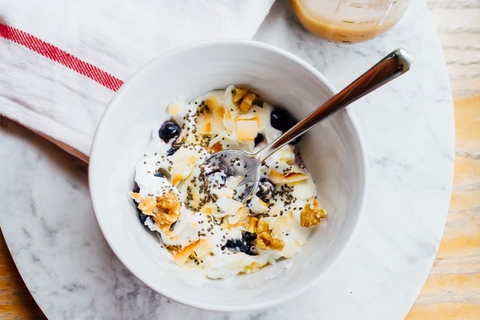 Yogurt Breakfast Bowl with Toasted Coconut, Walnuts, Blueberries and Chia with silver spoon in the bowl.